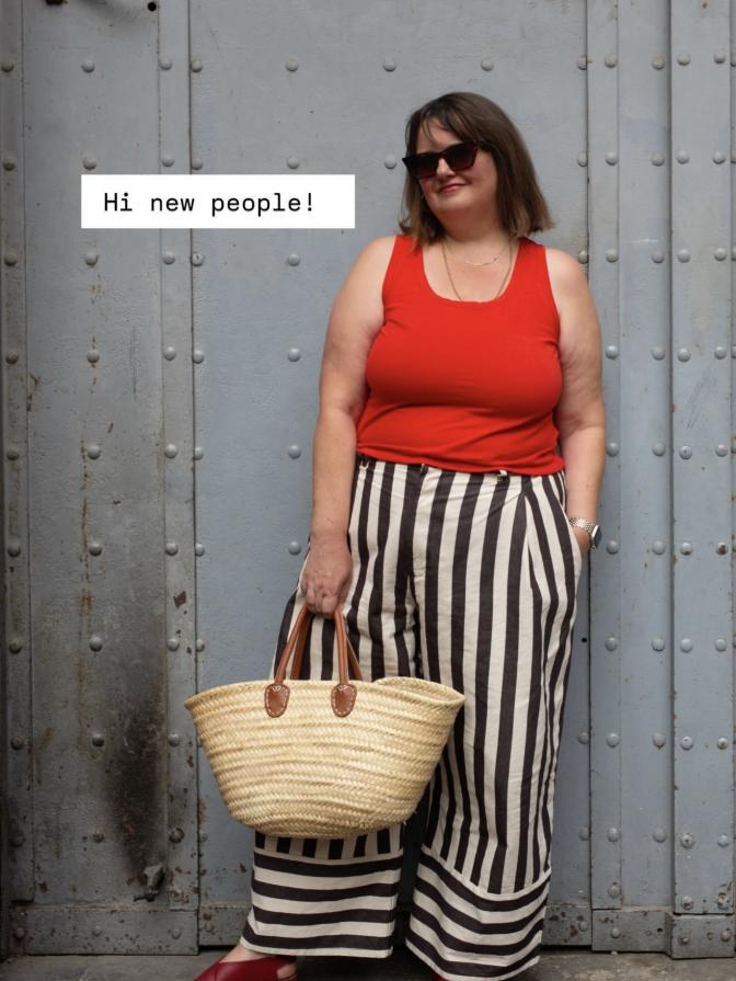 Elizabeth in a red tank top and striped trousers, holding a straw basket